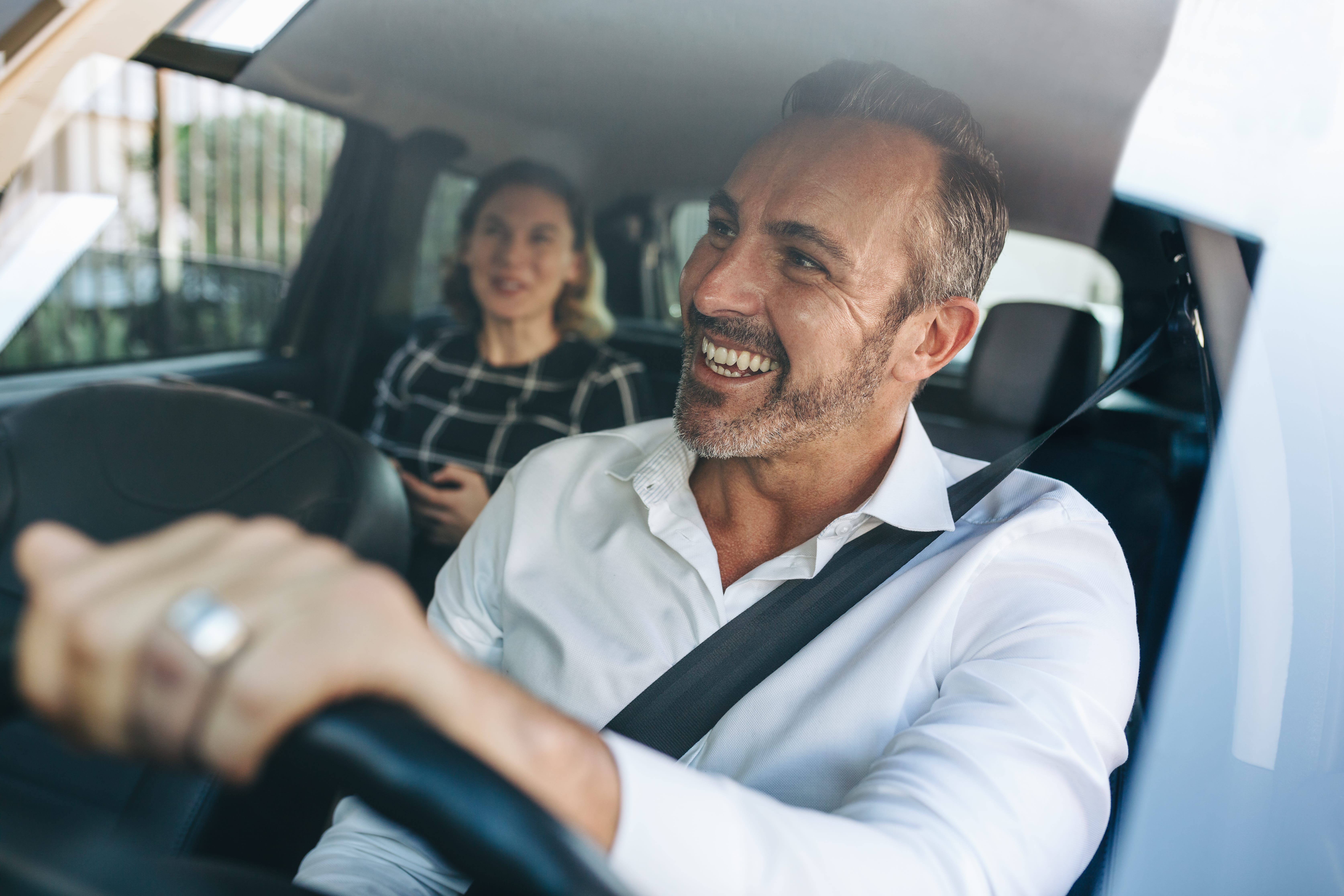 A man driving a car with a woman behind him.