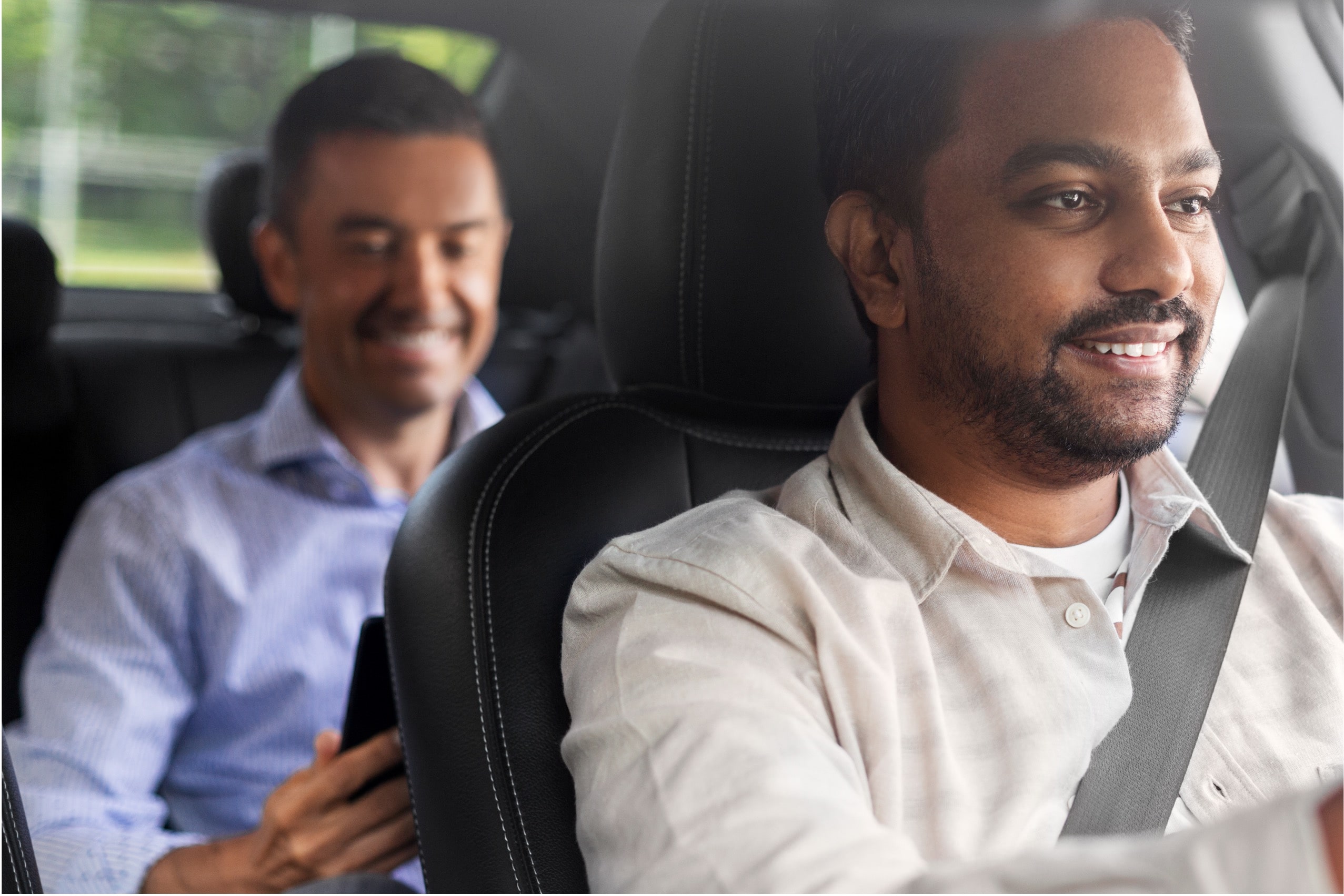 A man sitting in a car with another man behind him.
