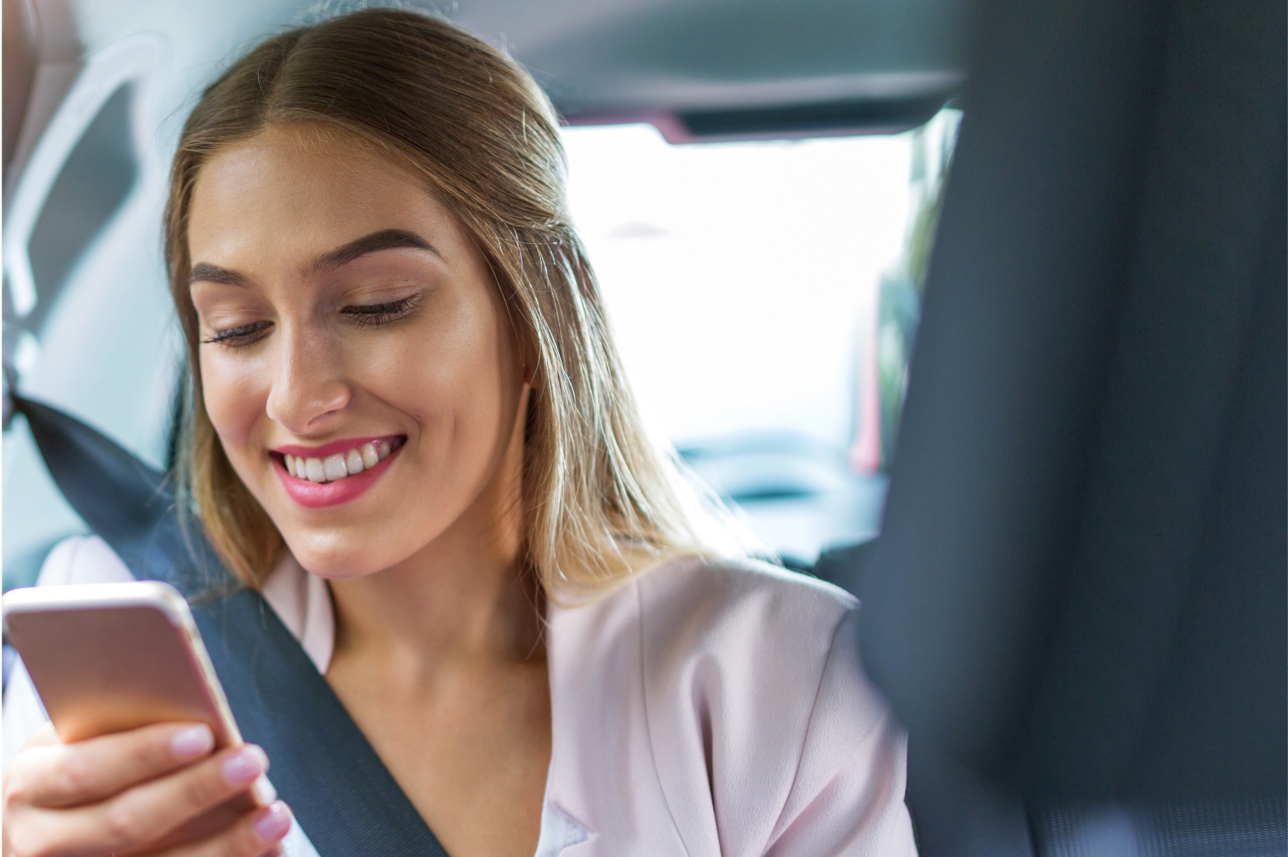A woman sitting in a car looking at her cell phone.