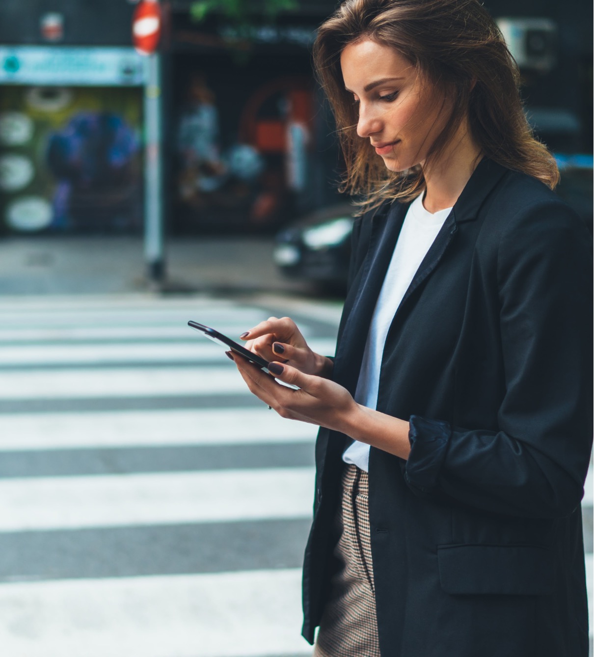 A woman standing on a street corner looking at her cell phone.
