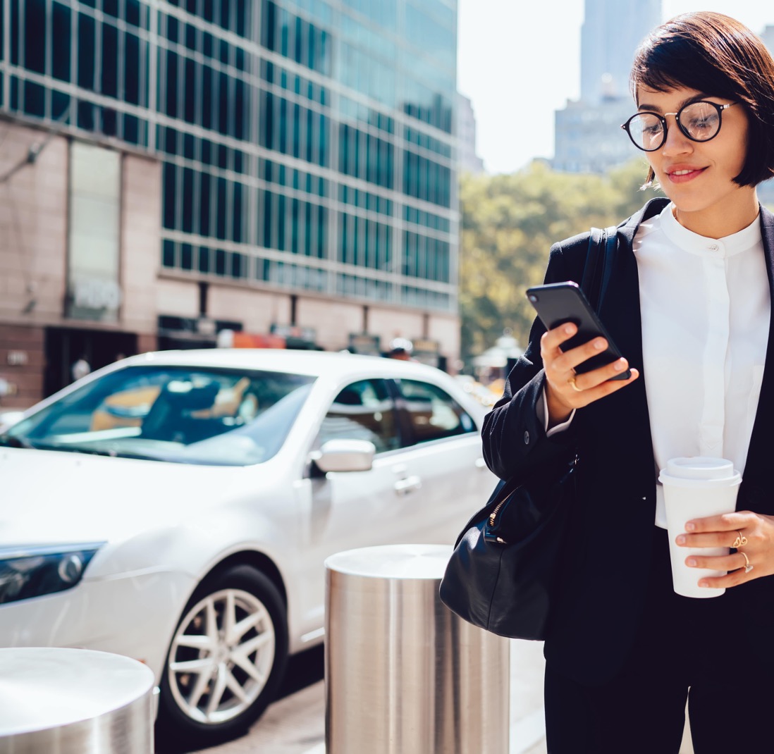A woman in a business suit holding a cup of coffee and looking at her phone.