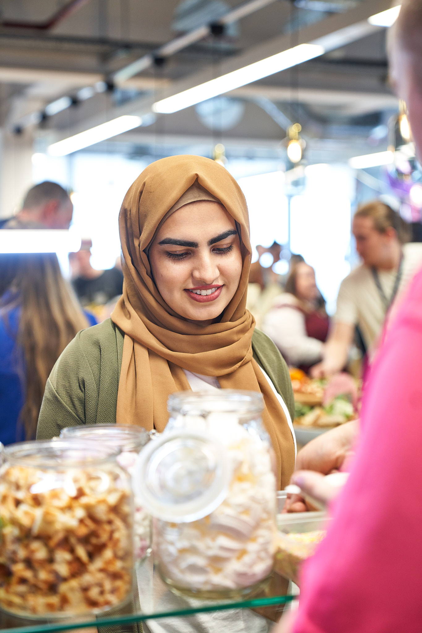 A woman in a hijab is looking at a jar of food.