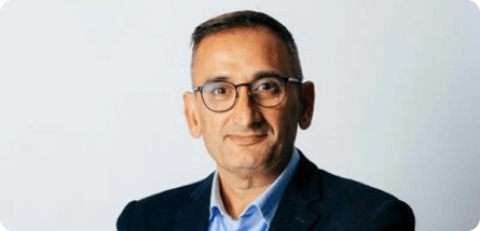 A man in a suit and glasses is smiling.