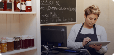 A woman in an apron is looking at a tablet.